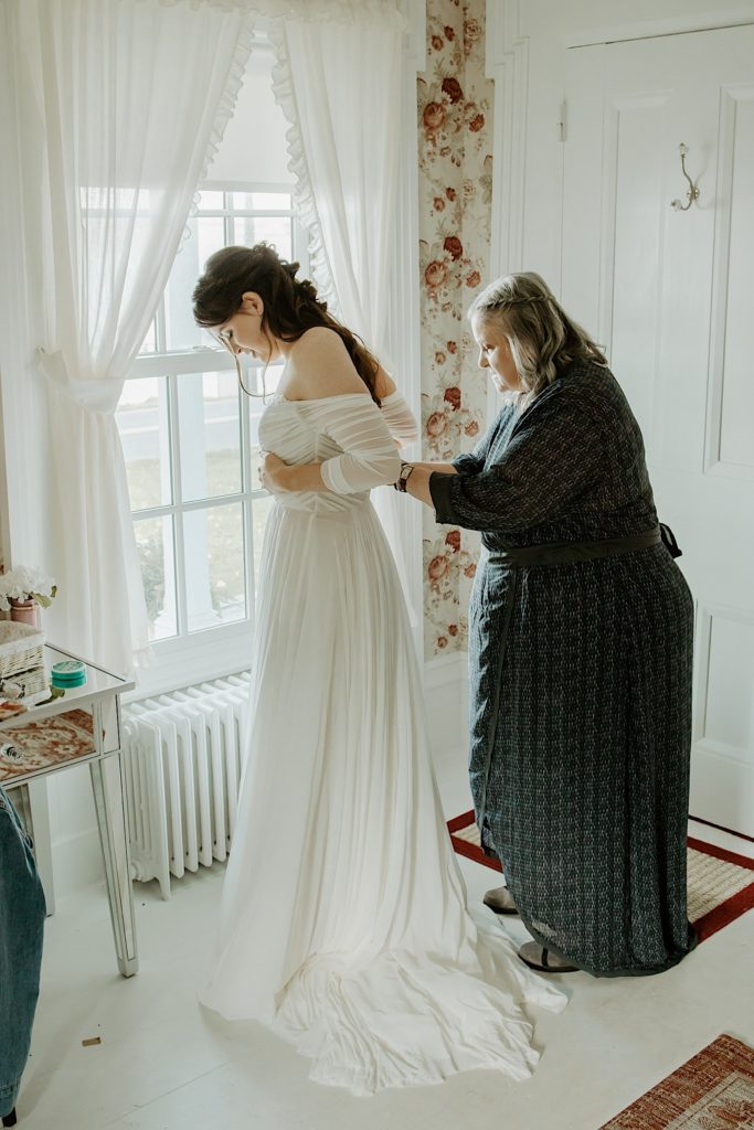 Mother helping bride put on wedding dress for intimate elopement at the Finger Lakes NY