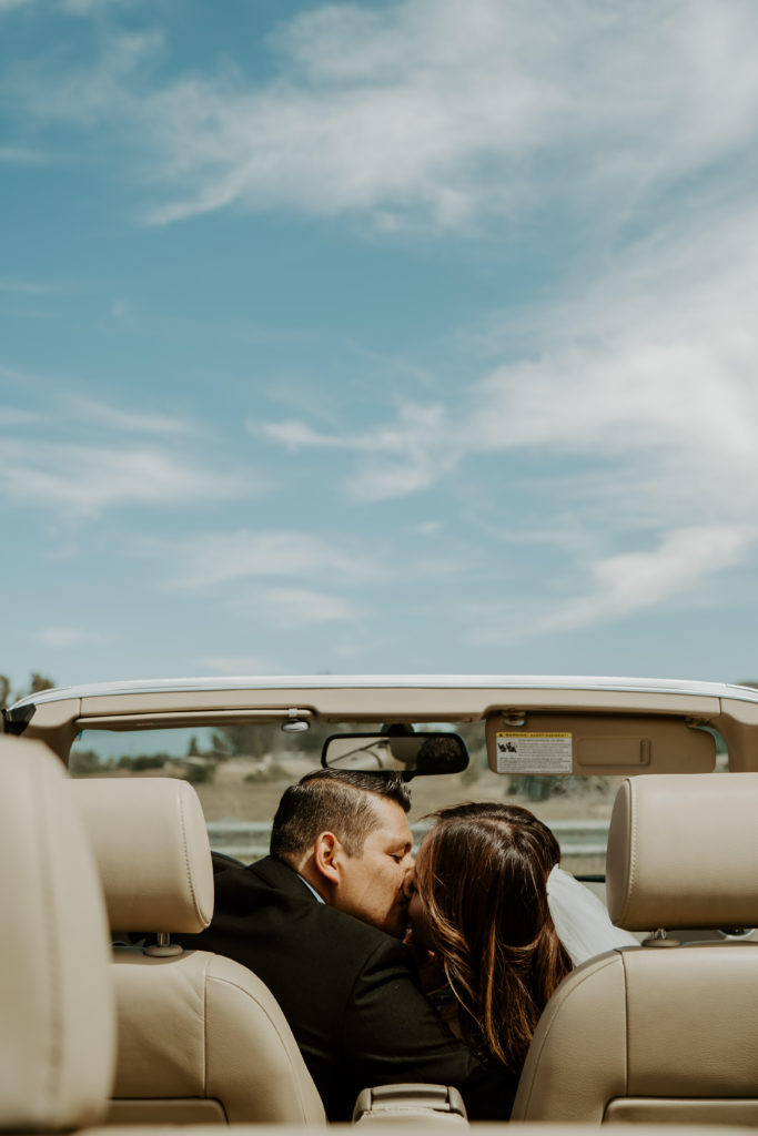 Newlyweds kiss while sitting in a convertible