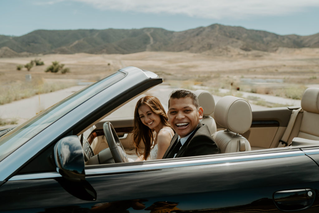 Newlyweds sitting in a convertible in the desert smiling and laughing during their adventure session