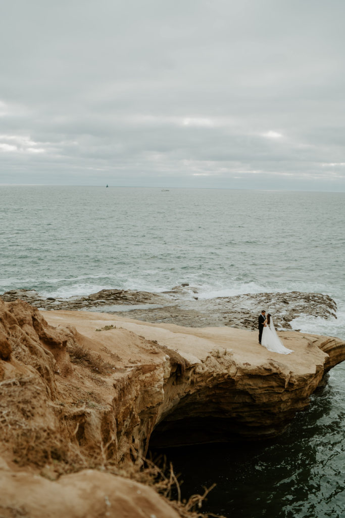 Bride and groom standing together on a small cliff with open water behind them