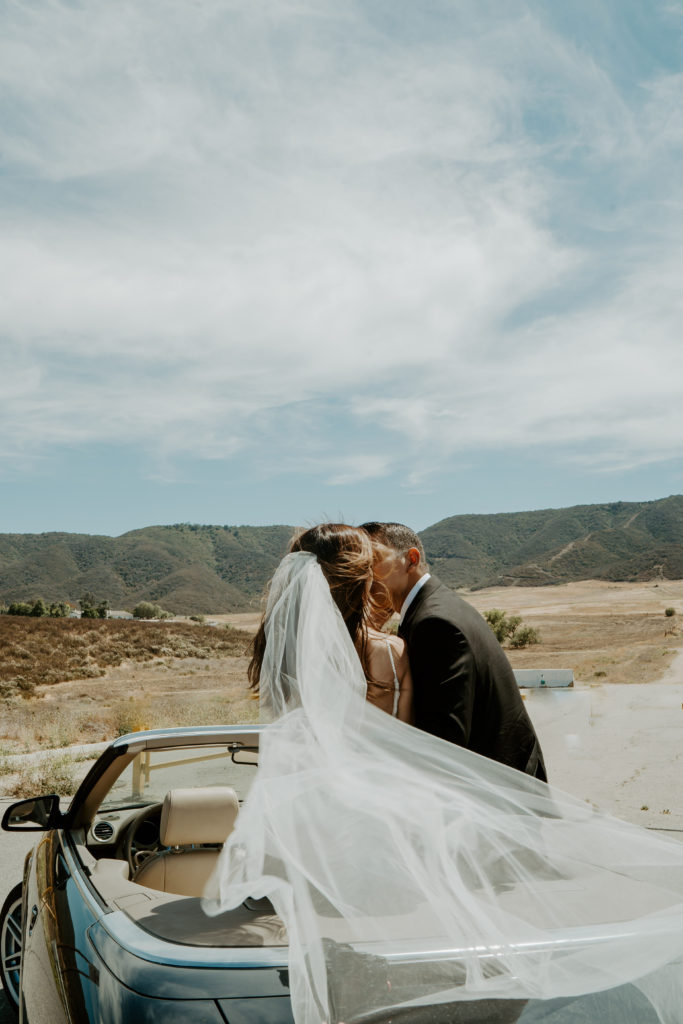 Bride and groom kiss sitting in a convertible in the desert