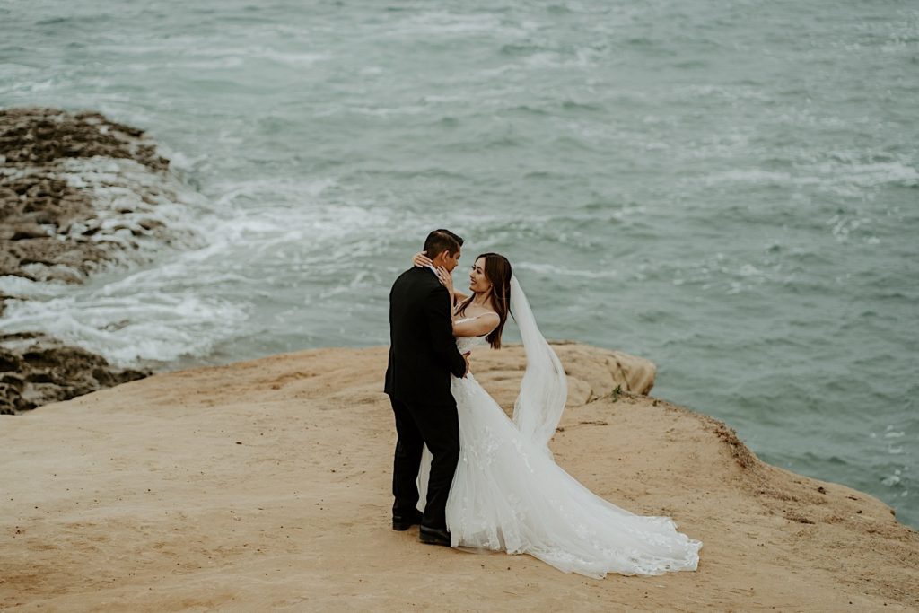 Bride and groom embrace in front of the open water