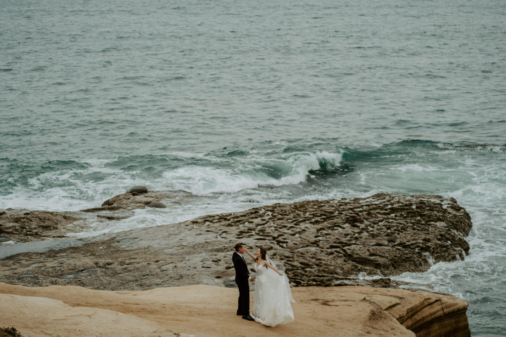 Bride and groom dance on a rock in front of open water during their adventure session