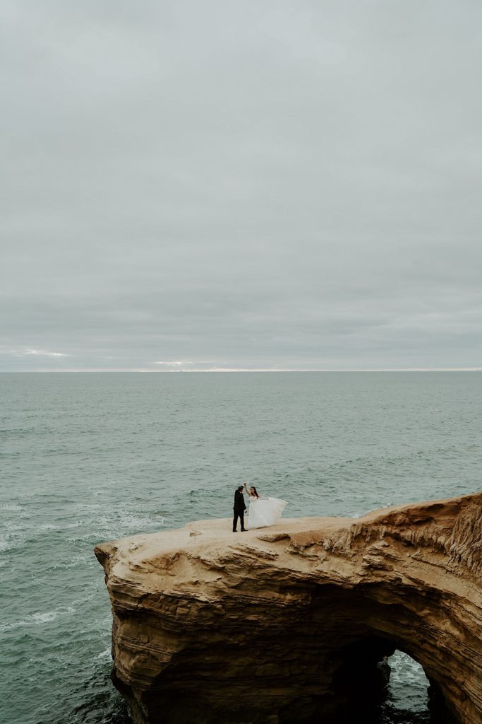 Bride and groom dance on rock platform above the open water