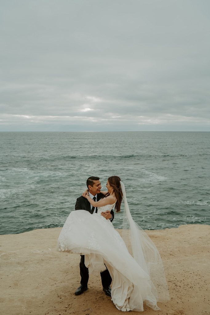 Groom holds bride in front of the open water