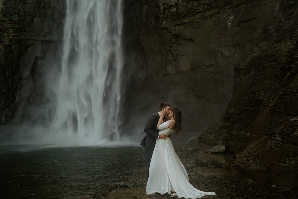 Bride and groom kiss next to waterfall during intimate elopement at the Finger Lakes NY