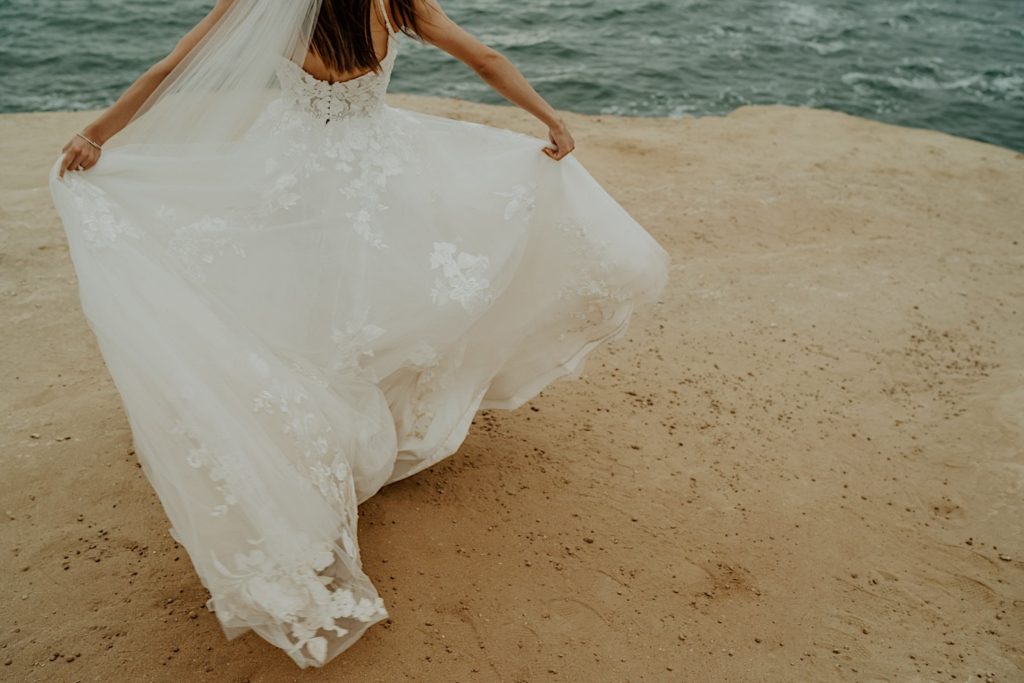 Bride's dress flowing as she runs towards the water