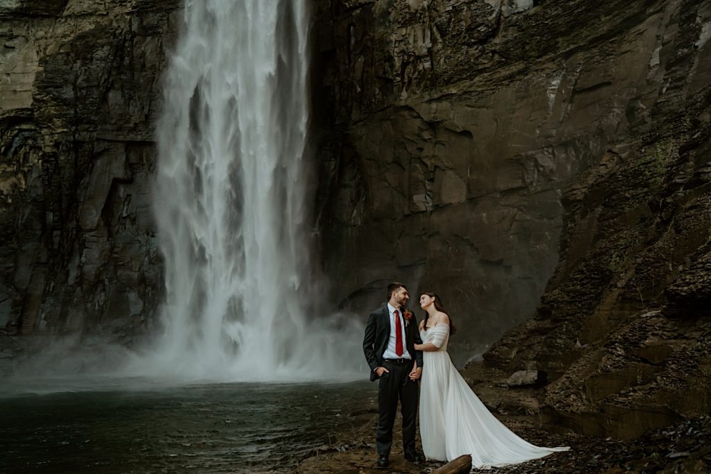 Bride holding grooms arm while standing in front of water fall for their intimate elopement in the Finger Lakes NY