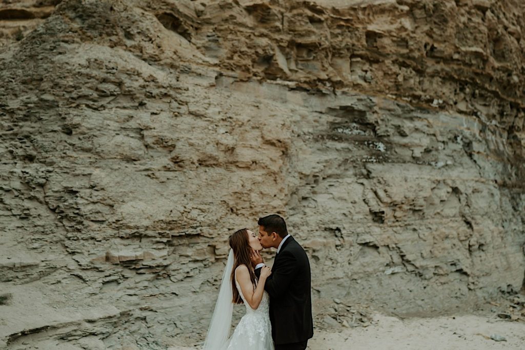 Bride and groom kiss in front of a rock wall
