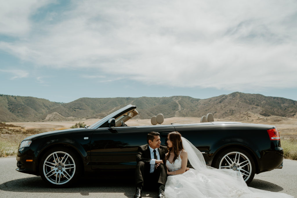 Newlyweds sit in front of a convertible in the desert for their adventure session