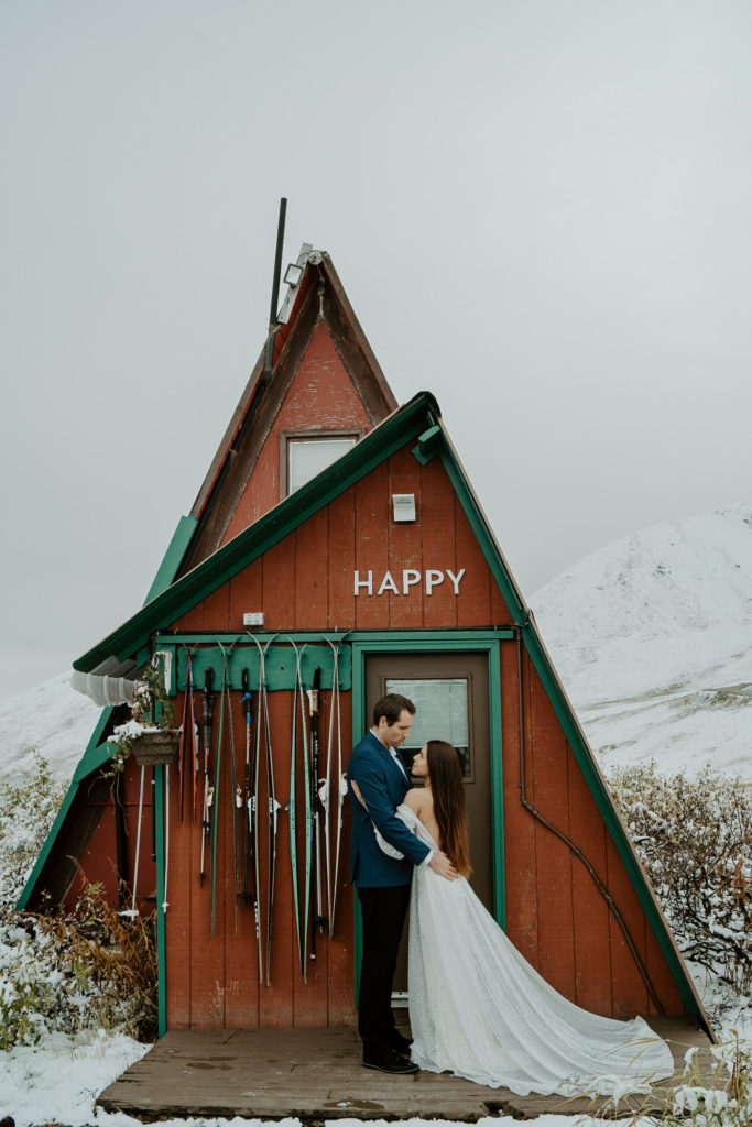 Husband and bride hug in front of Alaska cabin after elopement