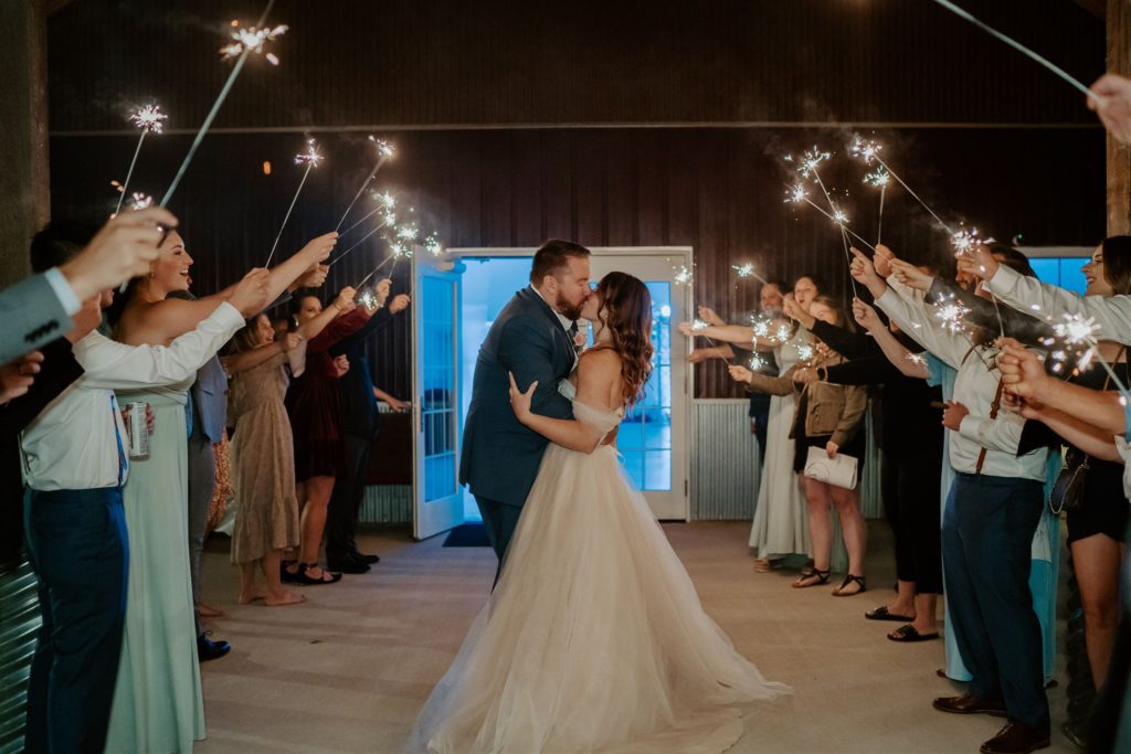Bride and groom kiss with their friends and family surrounding them with sparklers