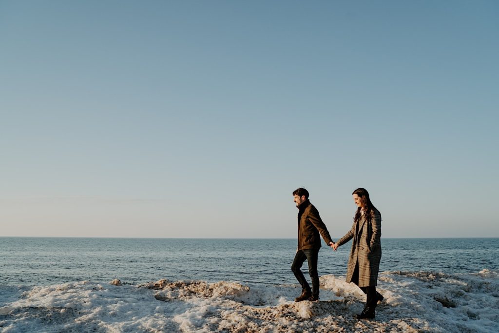 Couple walking along snowy beach of the Indiana dunes holding hands during their session