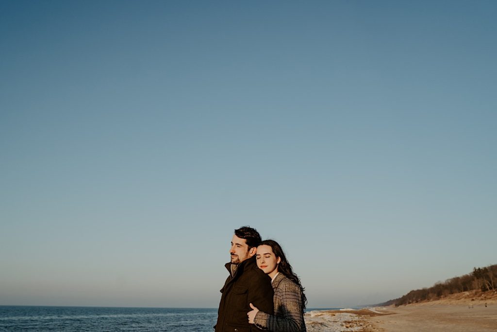 Woman embraces boyfriend from behind while standing on the beach