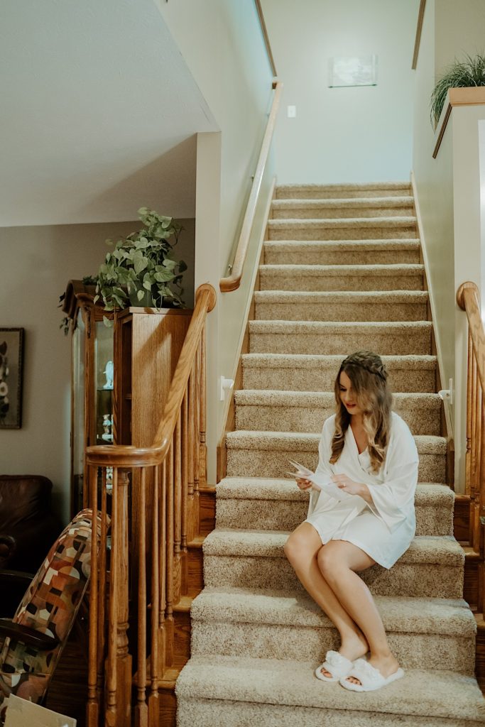 A bride sits on a staircase reading a letter from her soon to be husband before her wedding