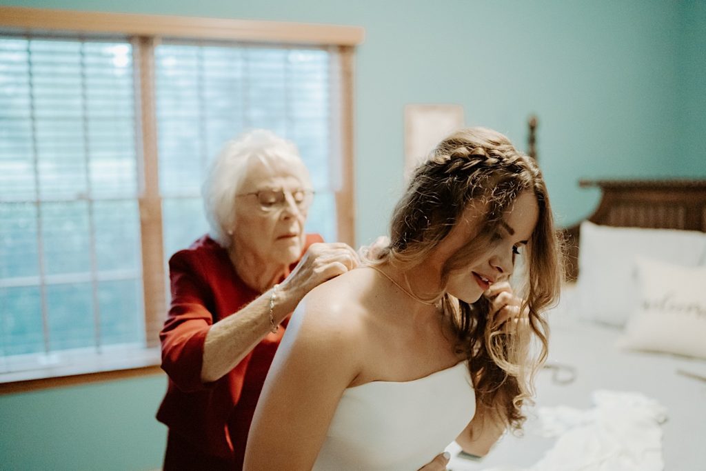 A grandma helping to put a necklace on a bride in a bedroom before her wedding
