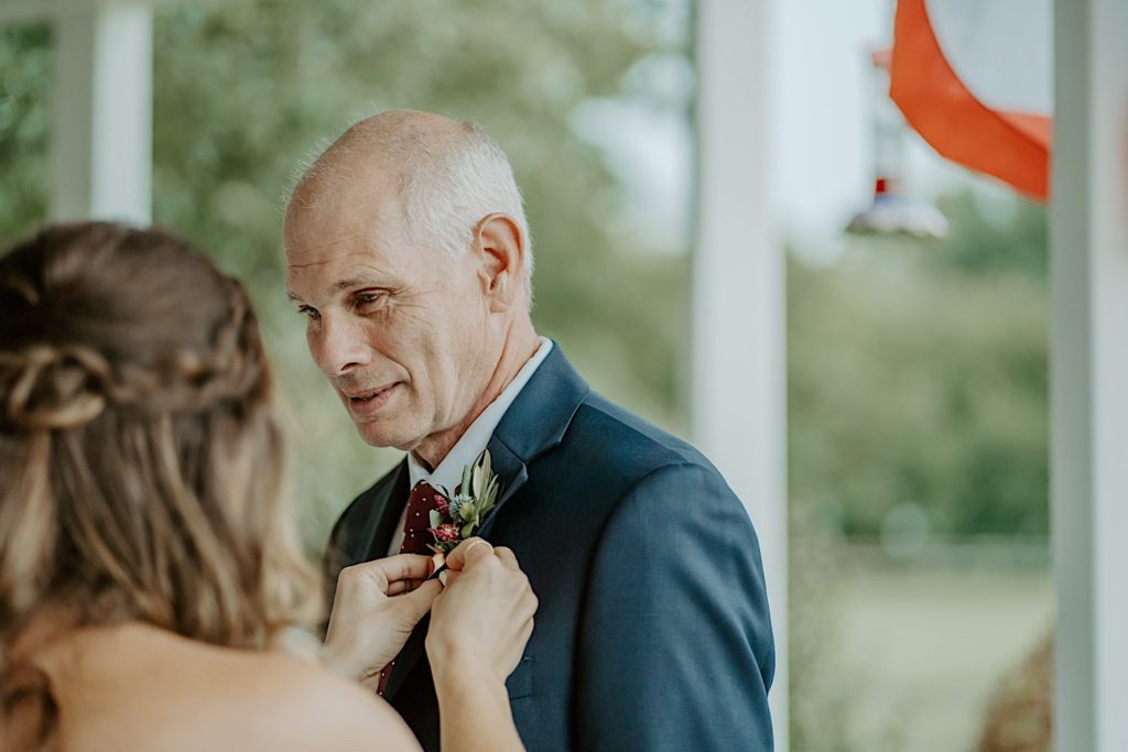 A bride helps to pin a corsage to her fathers coat
