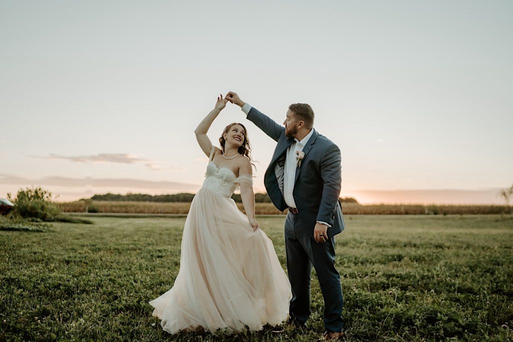 Newly weds dance in a field outside of their wedding venue, groom spins the bride
