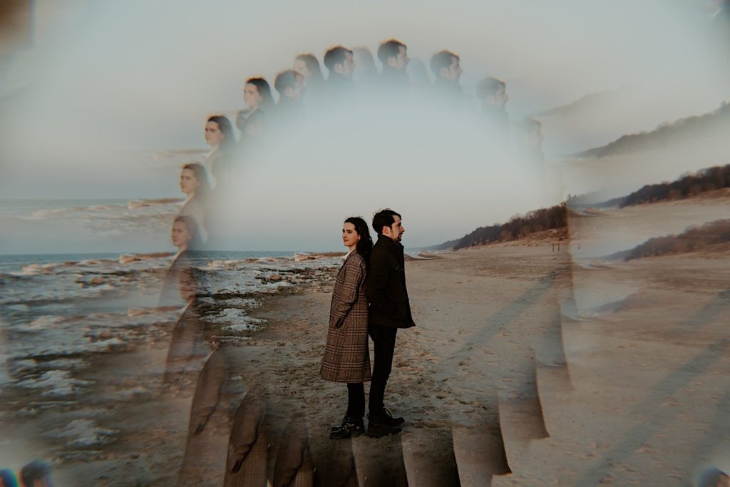 Couple stand back to back on the snowy beach of the Indiana Dunes during their session, photographed through a prism