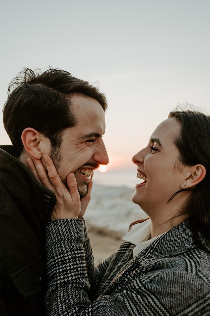 Woman holds mans face as they both laugh with the sun in the background
