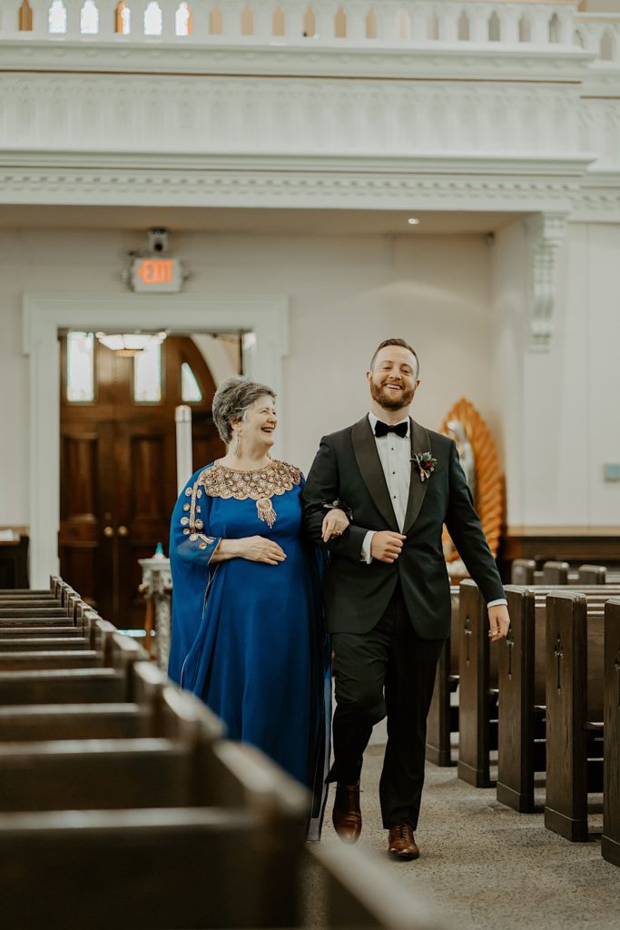 Groom and his mother walk down the aisle of a church for his wedding