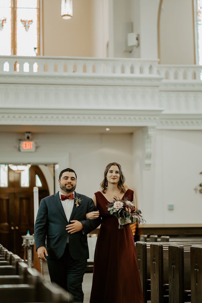 Groomsman and bridesmaid walk down the aisle of a church together