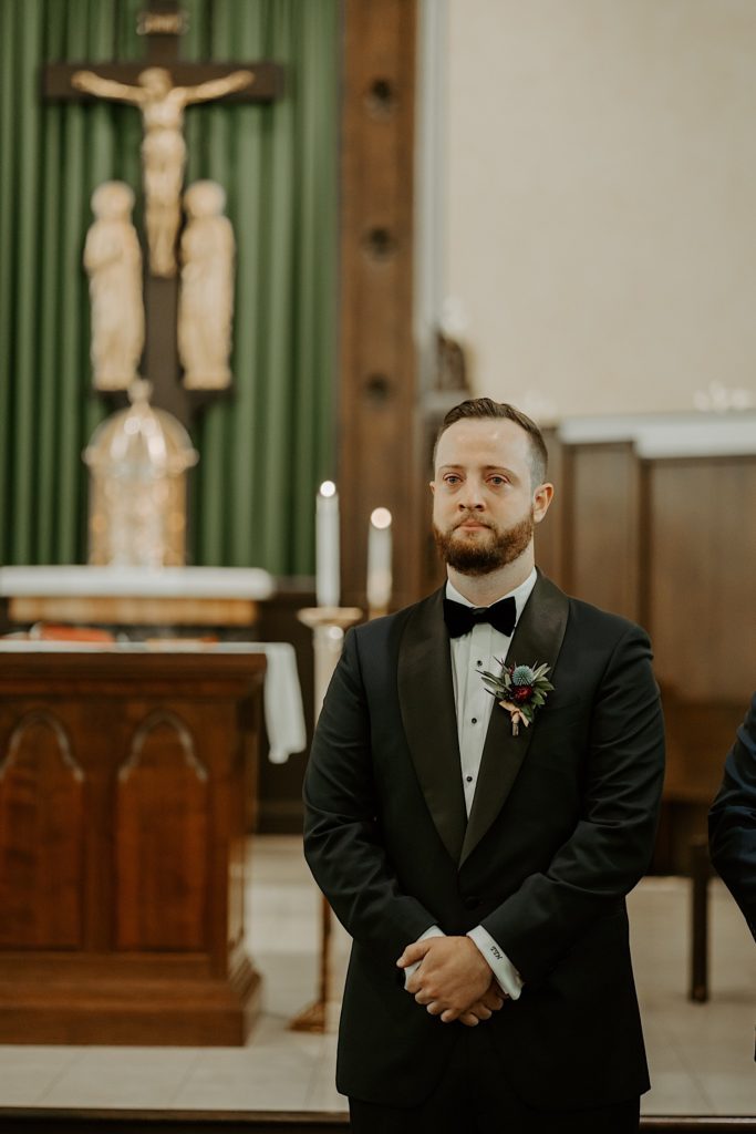 Groom stands holding his hands waiting for his bride to walk down the aisle of the church