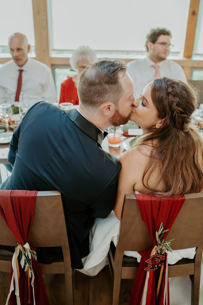 Bride and groom kiss while seated at their wedding reception table