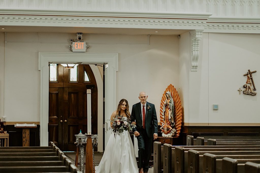 Father walks his daughter down the church aisle for her wedding ceremony
