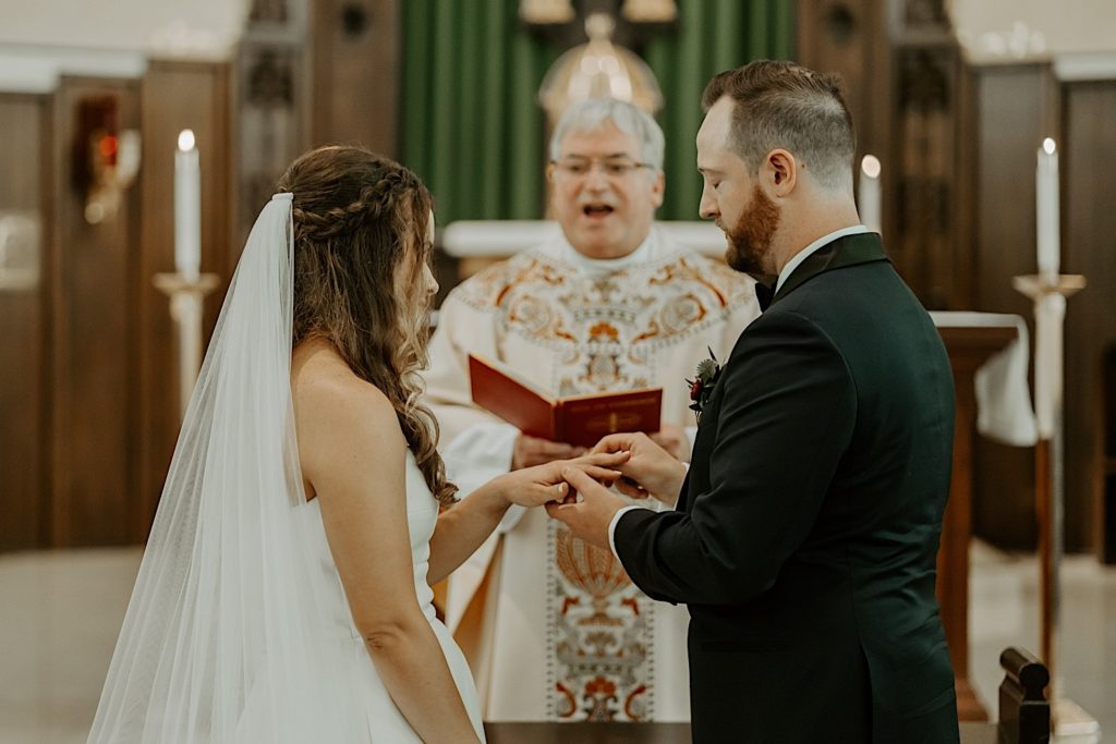 Bride and groom exchanging rings while the priest instructs them