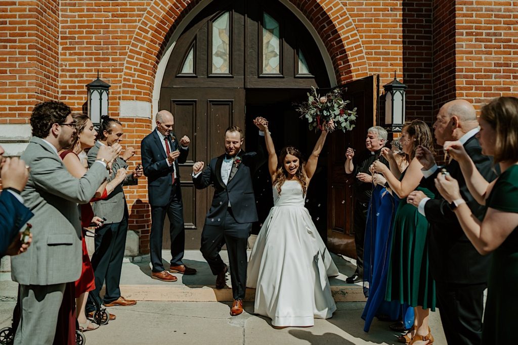 Bride and groom celebrate and exit a church as their family is gathered outside to celebrate with them