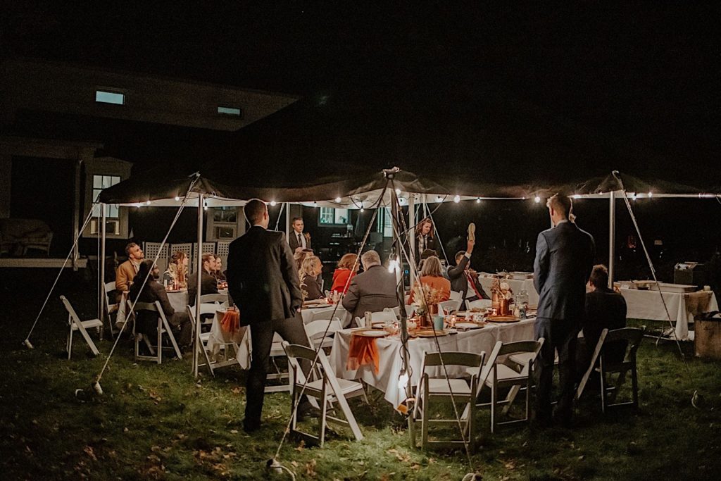 Wedding reception underneath a lit up tent at night with guests seated and standing
