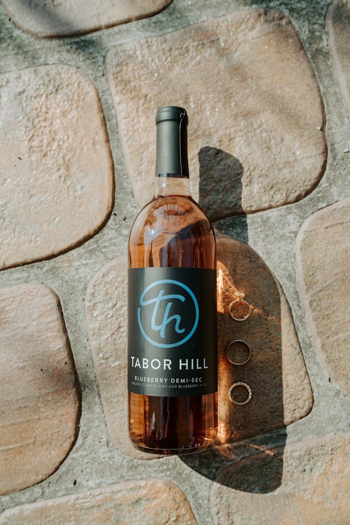 A wine bottle on the ground with 3 rings next to it, the bottle reads "Tabor Hill Blueberry Demi-sec"