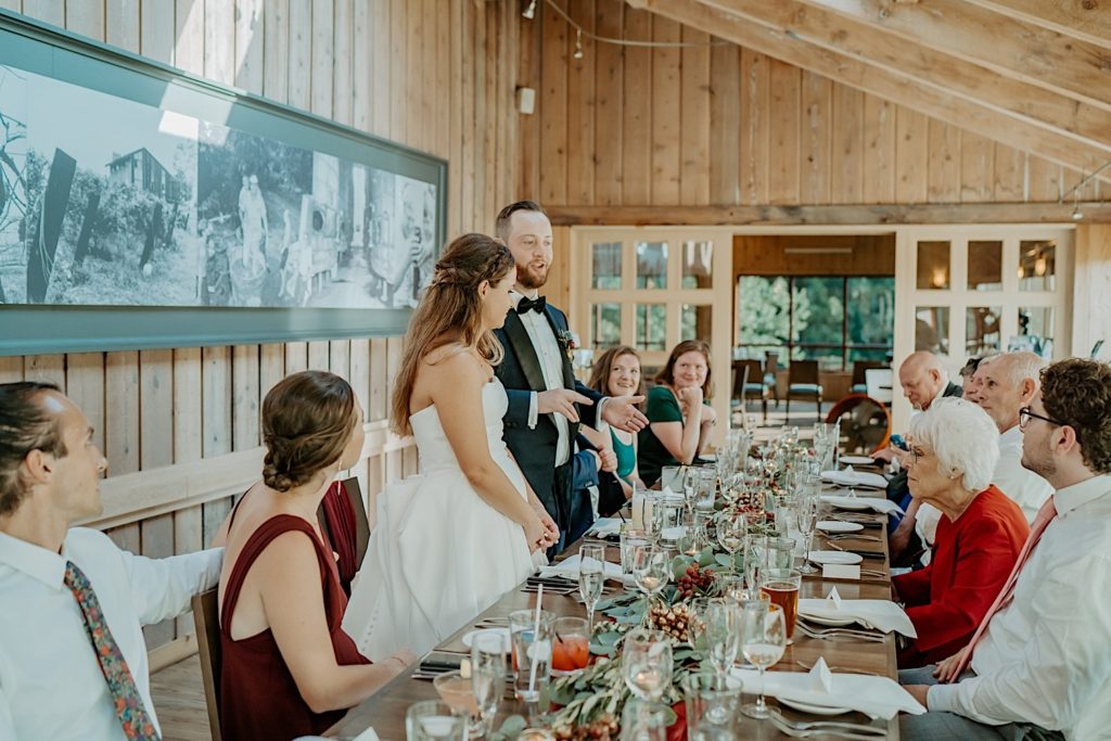 Bride and groom stand at their wedding reception while their guests stay seated at their table and watch