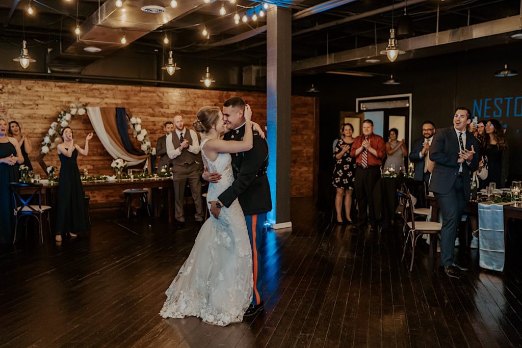 Bride and groom share first dance in their wedding venue with their guests watching