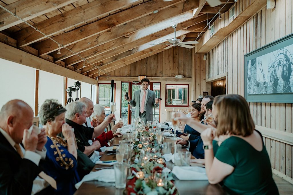 Groomsmen gives a speech at a wedding reception as the bride, groom, and guests toast