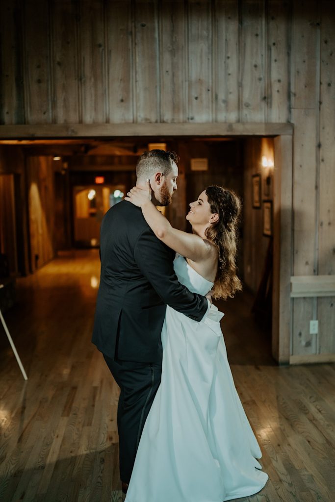 Bride and groom share their first dance together smiling at each other in front of a long hallway