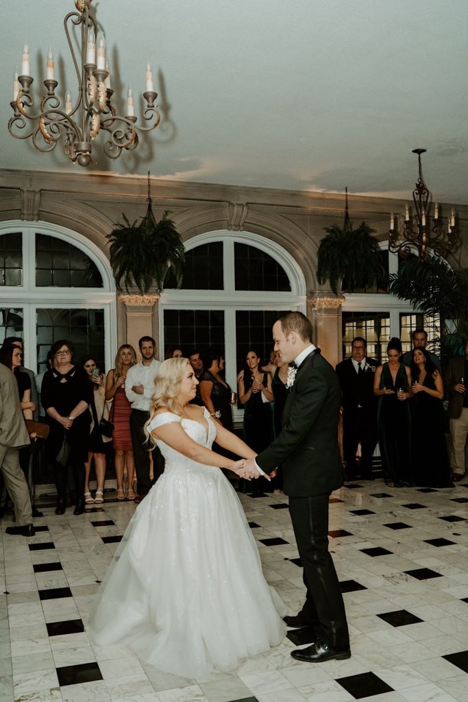 Bride and groom share first dance in their wedding venue with their guests watching