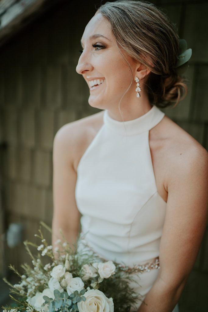 Bride smiles and holds a flower bouquet in front of a wood building