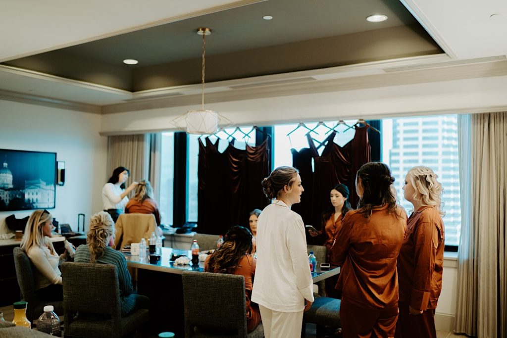 Wife and bridesmaids mingle in their getting ready space as they prepare for the wedding day. The bride is wearing while while the others are all wearing orange