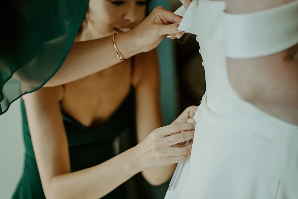 Bridesmaids helping button up a brides wedding dress