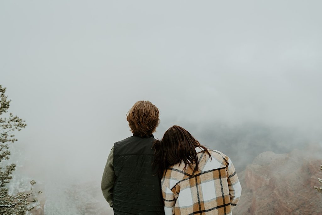 Woman rests her head on mans shoulder as they look at the fog with their backs turned to the camera