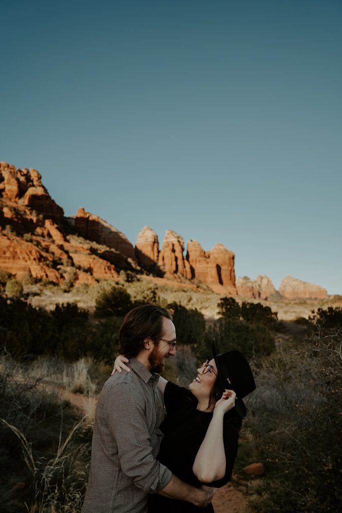 A couple embrace and smile at one another with Sedona red rocks in the background
