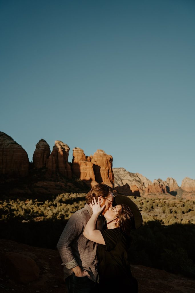 A newly engaged couple kiss one another with Sedona red rocks in the background