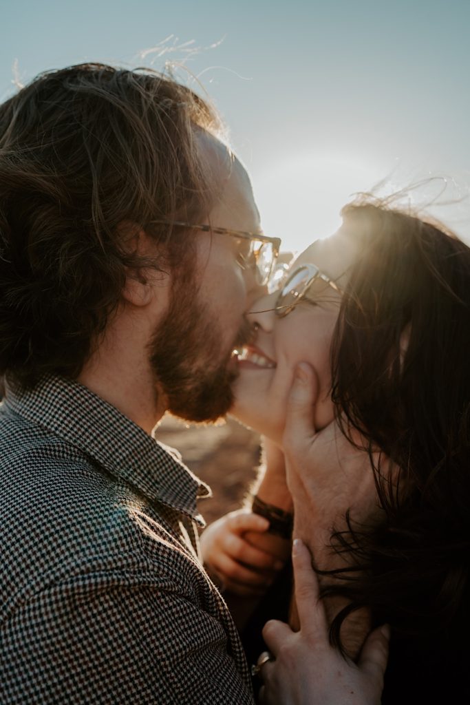 Close up of a man and woman kissing with the sun rising directly behind them