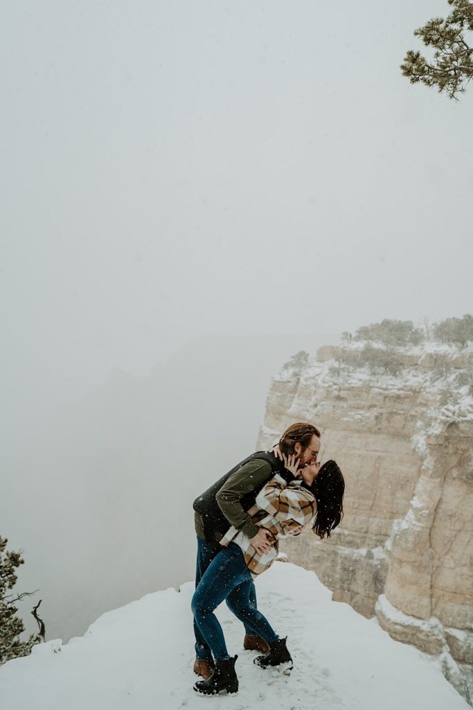 A couple kiss in front of a snow covered Grand Canyon