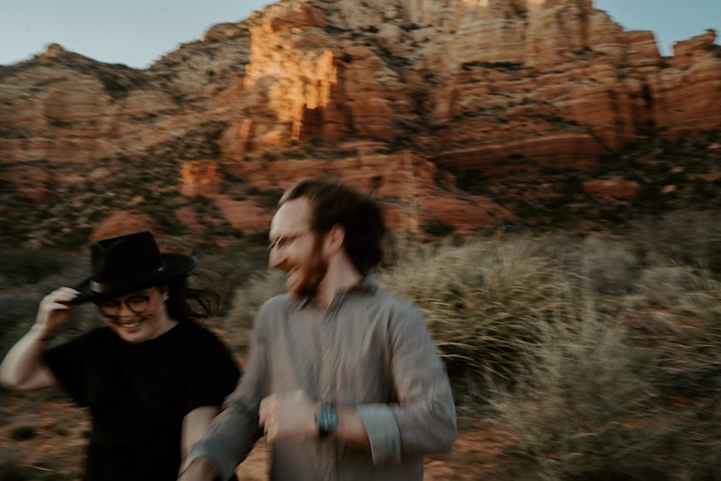 Blurry photo of a man and woman running and laughing in the desert in front of the Sedona red rocks