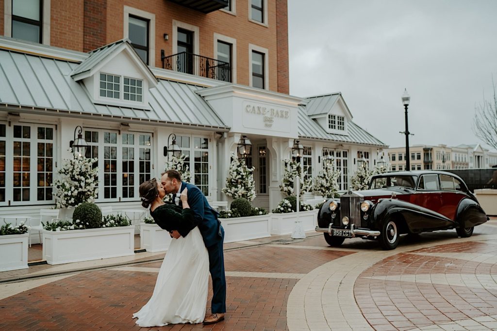 Bride and groom kiss in front of the Cake Bake Shop in Indiana with an old Rolls Royce in the background