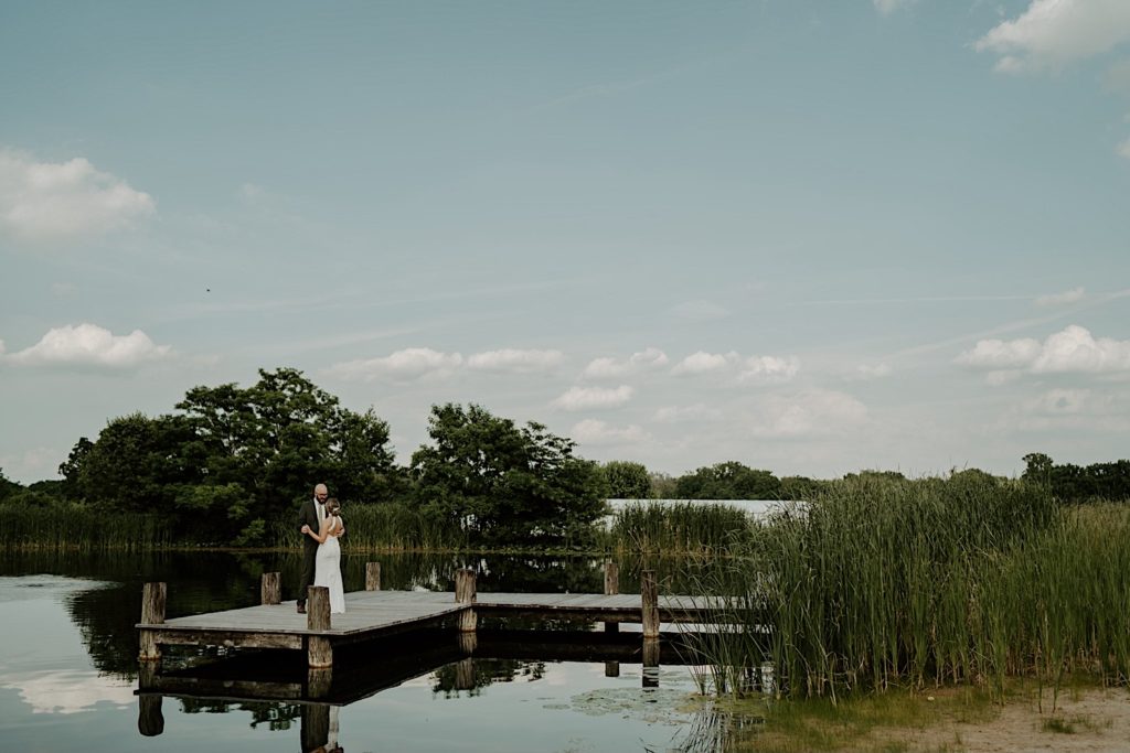 Bride and groom standing on a dock on the lake embracing and looking at one another