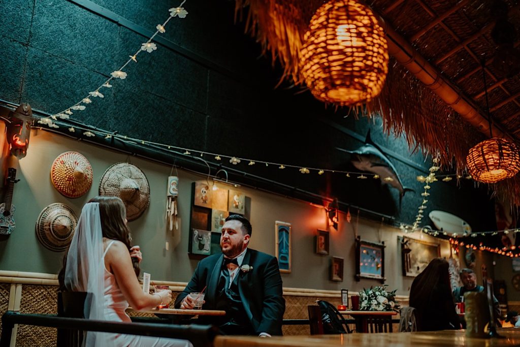 Bride and groom seated looking at one another in a sea themed bar with a swordfish on the wall
